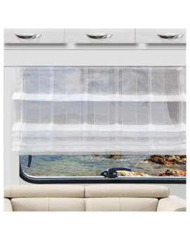 Ein durchsichtiger weißer Vorhang verdeckt ein breites Fenster, das sich über einem beigen Sofa befindet. Aus dem Fenster blickt man auf eine felsige Küste und ruhiges blaues Wasser. Über dem Fenster sind weiße Schränke mit silbernen Griffen angebracht.