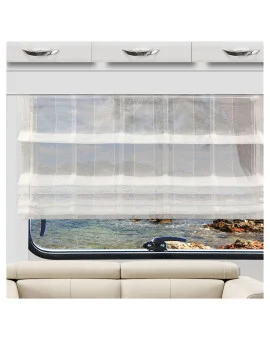 Ein durchsichtiger weißer Vorhang verdeckt teilweise ein großes Fenster mit Blick auf eine felsige Küste und ruhiges blaues Wasser. Über dem Fenster sind weiße Schränke mit silbernen Griffen angebracht, während sich darunter ein beiges Sofa befindet.