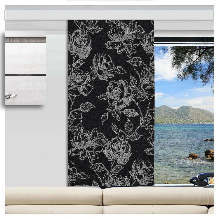 In einem Caravan steht ein weißes Sofa, das auf ein großes Fenster ausgerichtet ist. Das Fenster ist teilweise von einer dunklen Platte mit einem hellen Blumenmuster verdeckt. Durch das Fenster sind blaues Wasser, felsige Gebiete und grüne Hügel unter einem teilweise bewölkten Himmel zu sehen.