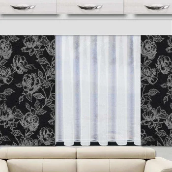 Ein Wohnwagen hat ein Fenster mit durchsichtigen weißen Vorhängen, die teilweise geöffnet sind. Das Fenster wird von schwarzen Vorhängen mit einem auffälligen weißen Blumenmuster eingerahmt. Über dem Fenster sind weiße Schränke mit silbernen Griffen angebracht, und darunter steht ein beiges Sofa.