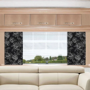 Ein beigefarbenes Sofa steht unter einem breiten Fenster mit weißen Vorhängen und Seitenteilen, die einen schwarzen Hintergrund und ein weißes Blumenmuster aufweisen. Über dem Fenster befinden sich helle Holzschränke mit silbernen Griffen. Durch das Fenster ist Grünzeug zu sehen.