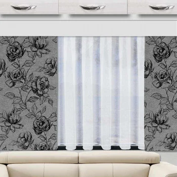 Ein cremefarbenes Sofa steht vor einem Fenster mit durchsichtigen weißen Vorhängen. Das Fenster wird von einer grauen Gardine mit einem großen schwarzen Rosenmuster eingerahmt. Über der Szene sind weiße Schränke mit silbernen Griffen angebracht.
