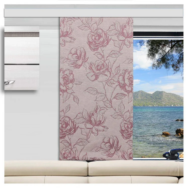 Ein Wohnmobil mit einem beigen Sofa vor einem großen Fenster. Vor dem Fenster ist ein rosafarbener, geblümter Vorhang teilweise zugezogen, der einen Blick auf blaues Wasser, felsige Küste, Baumzweige und ferne grüne Hügel unter einem klaren Himmel freigibt.