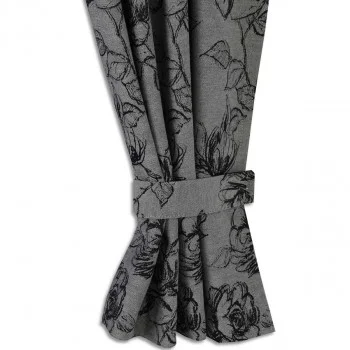 Nahaufnahme eines grauen Vorhangs mit schwarzem Blumenmuster, der gerafft und mit einem passenden Raffhalter befestigt ist. Der Stoff zeigt skizzierte Umrisse von Blumen und Blättern, mit präzisen Details, die im gesamten Design sichtbar sind.