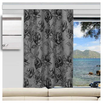 Ein grauer Vorhang mit einem schwarzen Blumenmuster ist vor einem Wohnwagenfenster teilweise geöffnet. Durch das Fenster sind blaues Wasser, ein felsiges Ufer, ferne grüne Hügel und ein Baumzweig zu sehen. Direkt unter dem Fenster steht ein beiges Sofa.