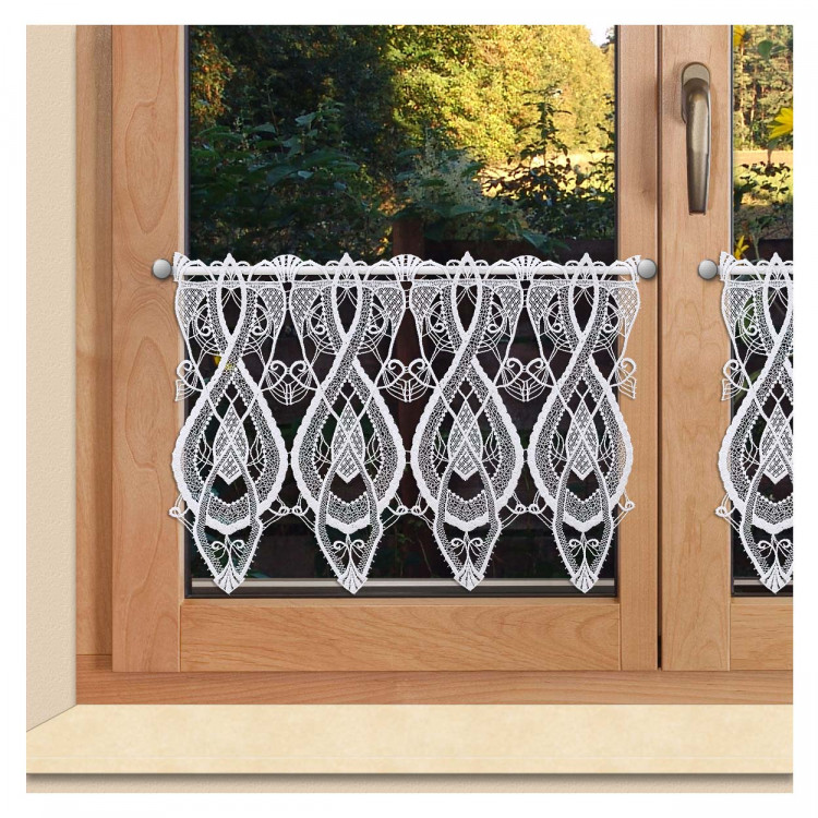 Ein holzgerahmtes Fenster mit zwei Glasscheiben ist mit einem kurzen weißen Spitzenvorhang mit einem komplizierten, symmetrischen Muster versehen. Eine silberne Gardinenstange hält den Vorhang. Durch das Glas sind grüne Bäume zu sehen.