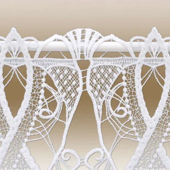 Weiße Spitze mit geometrischen und floralen Mustern hängt an einer Stange vor einem beigen Hintergrund. Die Spitze besteht aus verflochtenen Linien, Blattformen und feinen Netzelementen, die eine detaillierte handwerkliche Verarbeitung der Muster zeigen.