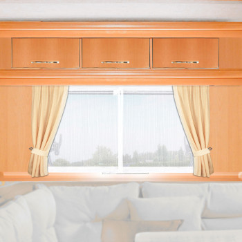 Helle Holzschränke mit drei Schubladen sind über einem Fenster angebracht. Auf beiden Seiten des Fensters sind cremefarbene Vorhänge aufgespannt, durch die verschwommenes Grün und der Himmel zu sehen sind. Unter dem Fenster befindet sich ein teilweise sichtbares weißes oder hellbeiges Sofa mit Polstern.