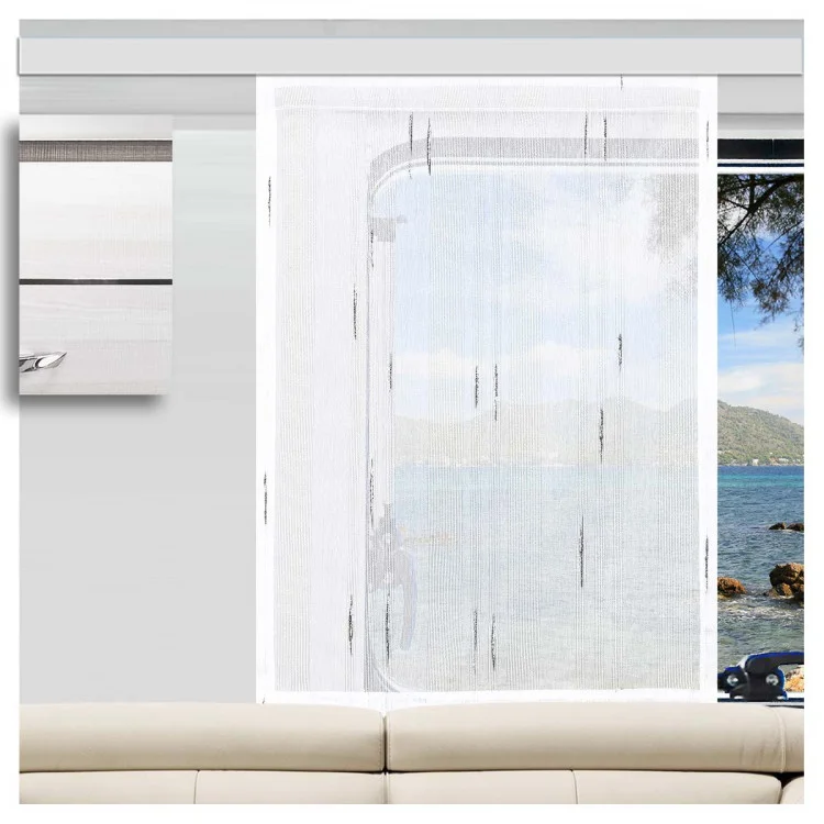 Die Caravan-Schiebegardine „Alva“ in Weiß-Anthrazit von SeGaTeX Home Fashion hängt vor einem Wohnwagenfenster, hinter dem sich Berge, Wasser und Bäume erstrecken. Daneben steht ein beiges Sofa.