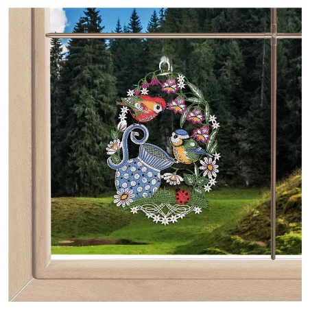 „Fensterbild Hibiskusblüte lila“ von ANDEA design, eine zarte Fensterdekoration aus Spitze, hängt vor dem Fenster, hinter dem sich ein Wald und eine Wiese erstrecken.