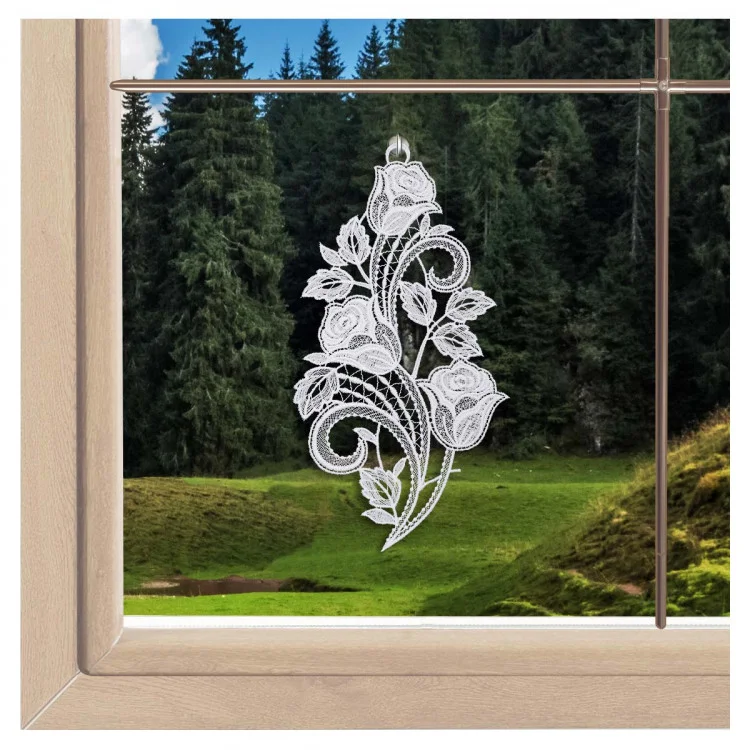 Das Dekor „Fensterbild Rosentraum Sekt“ ist in einem Fenster mit Holzrahmen abgebildet, wodurch die drei Rosenblüten aus Spitze vor dem Hintergrund eines üppigen Waldes besonders zur Geltung kommen.