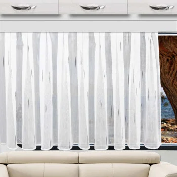 Über einem beigen Sofa hängt ein transparenter Scherli-Vorhang aus der „Caravanstore Alva“-Kollektion von SeGaTeX; durch das Fenster sind Bäume zu sehen, und über dem Sofa sind Schubladen angebracht.