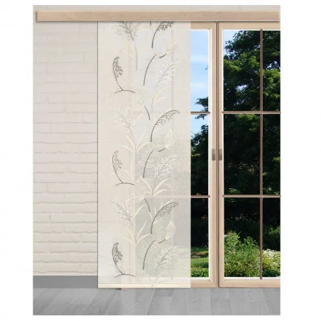 Ein halbtransparenter Vorhang mit einem zarten botanischen Muster hängt vor einem großen Fenster mit einem Holzrahmen, der den Blick auf einen grünen Garten und Bäume freigibt. Der Raum hat weiße Backsteinwände und einen hellgrauen Fußboden.