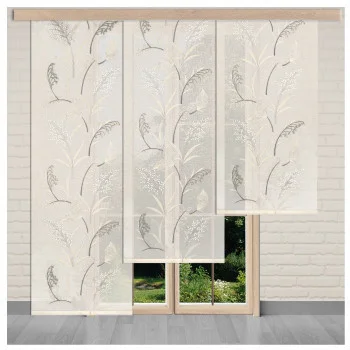 Vier durchsichtige, sektfarbene Flächenvorhänge mit dezentem Blumenmuster hängen vor einem Fenster. Die Paneele überlappen leicht, so dass natürliches Licht hindurchfällt und der Blick auf das Grün draußen frei wird. Der Raum hat eine helle Ziegelwand und einen grauen Boden.