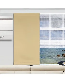 Ein beiger Vorhang verdeckt den linken Teil eines großen Fensters, das sich über einem cremefarbenen Sofa befindet. Der rechte Teil des Fensters ist unbedeckt und offenbart einen durchsichtigen Vorhang und einen Blick nach draußen, der Wasser, Felsen und blauen Himmel umfasst.