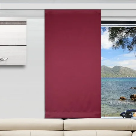 Ein modernes Wohnzimmer mit einem cremefarbenen Sofa, einem weinroter Vorhang, der ein großes Fenster teilweise verdeckt, und einem Blick nach draußen auf das Meer mit Bergen und Bäumen. An der linken Wand hängt ein weißes und graues abstraktes Kunstwerk.