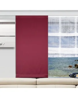 In einem modernen Wohnzimmer steht ein beigefarbenes Sofa vor einem Fenster mit zwei Paneelen: einem burgunderroten Paneel auf der linken Seite und einem transparenten Paneel auf der rechten Seite, durch das man einen Blick auf das Meer mit Felsen und Wellen hat. An der linken Wand ist ein silberner Schrank angebracht.