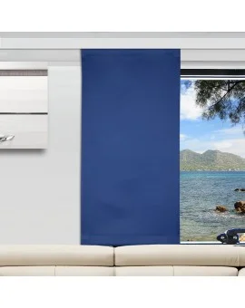 Ein modernes Wohnzimmer mit einem beigen Sofa und einem blauen Flächenvorhang, der ein Fenster teilweise verdeckt. Das Fenster bietet einen Blick auf ein ruhiges Meer, grüne Berge in der Ferne und einen klaren Himmel. Links neben dem Fenster befindet sich ein gerahmtes Wandkunstwerk.
