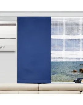 In einem modernen Wohnzimmer steht ein beiges Sofa vor einem Fenster. Die linke Seite des Fensters ist mit einem blauen Verdunkelungsvorhang bedeckt, während die rechte Seite mit einem weißen Vorhang verhängt ist, der den Blick auf das Meer, die Felsen und den Himmel freigibt.