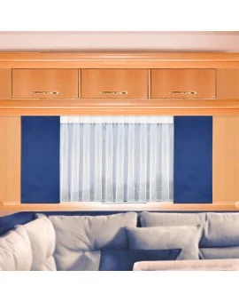 Ein heller Holzschrank mit drei Schubladen ist über einem Fenster angebracht, das mit weißen Vorhängen und dunkelblauen Seitenwänden verhängt ist. Ein helles Sofa mit Plüschkissen ist am unteren Bildrand teilweise sichtbar.