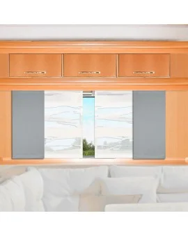 Ein Holzschrank mit drei Schubladen steht über einem Fenster mit zwei teilweise geöffneten grauen Jalousien. Außerhalb des Fensters sind Grünflächen und ein bewölkter Himmel zu sehen. Im Vordergrund befindet sich ein weißes Sofa mit weißen und hellgrauen Kissen.
