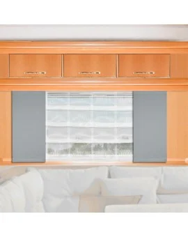 Ein heller Holzschrank mit drei Schubladen und Messinggriffen ist über einem Fenster angebracht, das mit durchsichtigen weißen Jalousien und grauen Seitenteilen ausgestattet ist. Unter dem Fenster steht ein weißes Sofa mit Plüschpolstern. Der Raum wirkt hell und modern.
