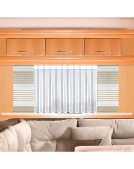 Innenansicht eines Wohnwagenfensters mit dem weißen Caravan-Store ANNA, kombiniert mit der beigen Flächengardine AIKO; moderne Fensterausstattung im Camper mit Holzschrank und gemütlicher Sitzecke.