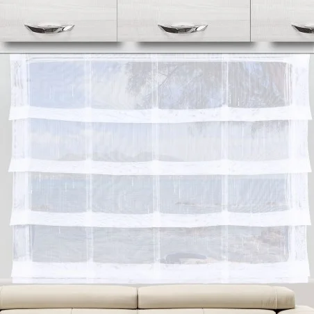 Ein durchsichtiger weißer Vorhang mit horizontalen Streifen ist vor einem großen Fenster angebracht, das viel Licht hereinlässt. Über dem Fenster sind moderne weiße Schränke mit silbernen Griffen angebracht. Ein Teil einer hellen, gepolsterten Bank erscheint am unteren Rand.