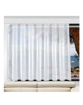 Maßgefertigter Caravan-Store ANNA in Weiß an einem Wohnwagenfenster mit Blick auf das Meer, eine felsige Küste und ein kleines Boot; im Vordergrund die Kante eines hellen Sofas im Wohnmobil-Innenraum.