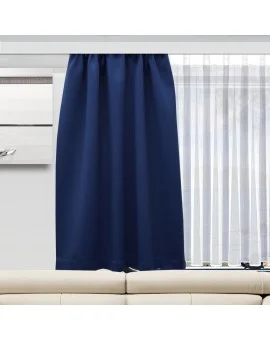 Ein dunkelblauer Vorhang verdeckt teilweise ein Fenster, dahinter befinden sich weiße Vorhänge, die Licht in den Raum lassen. Unter dem Fenster steht ein beiges Sofa, und auf der linken Seite des Bildes ist ein Teil eines Schranks mit einem silbernen Griff zu sehen.