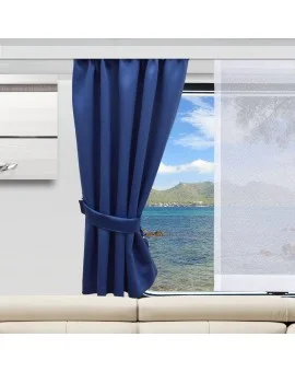 In einem modernen Raum stehen ein beiges Sofa, ein marineblauer Vorhang, der zur Seite gezogen ist, und ein durchsichtiger weißer Vorhang. Das Fenster gibt den Blick frei auf blaues Meerwasser, eine felsige Küste und weit entfernte grüne Hügel unter einem teilweise bewölkten Himmel.