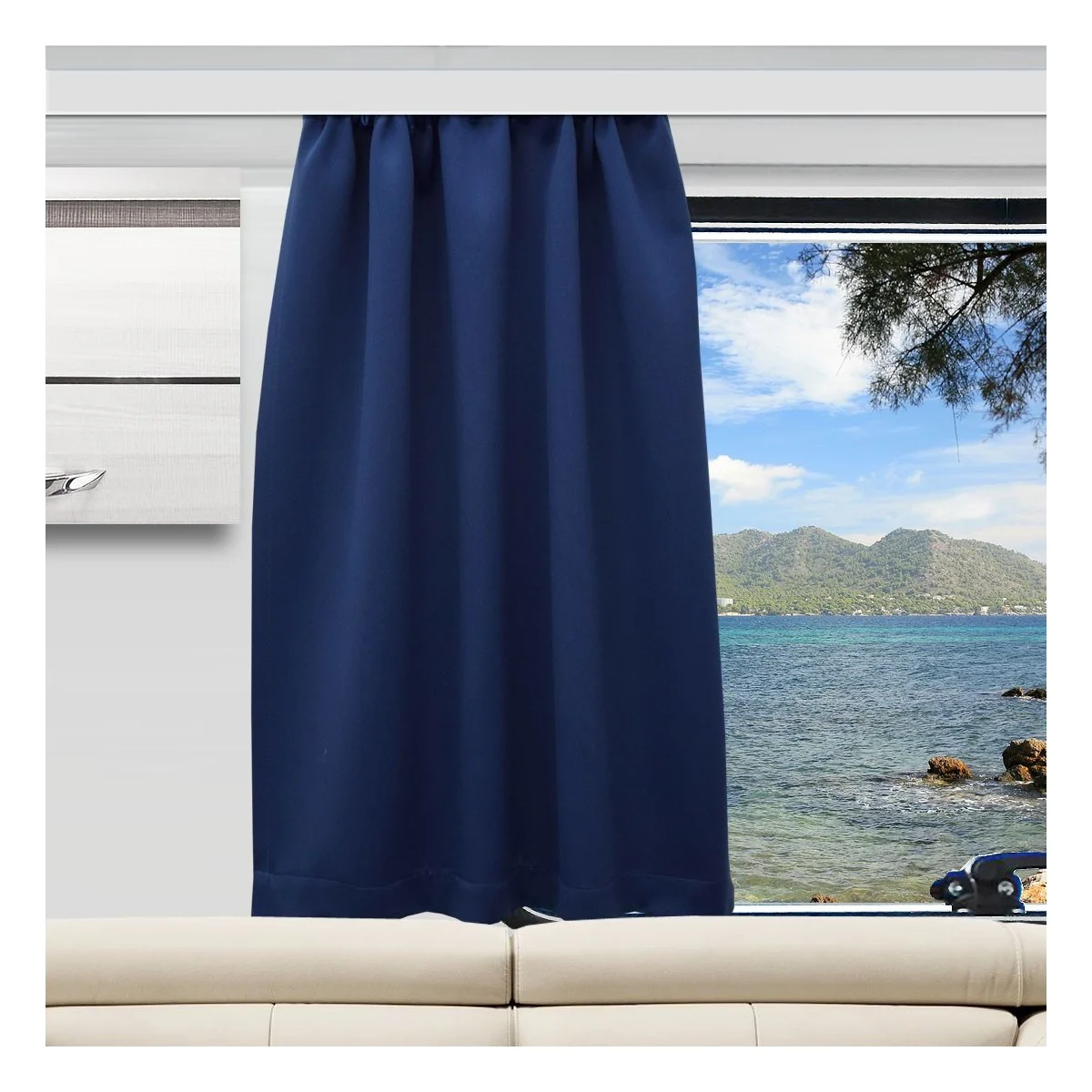 Ein dunkelblauer Vorhang verdeckt die Hälfte eines großen Fensters in einem modernen Wohnwagen. Durch das Fenster blickt man auf einen ruhigen blauen Ozean, Baumzweige und entfernte grüne Hügel unter einem teilweise bewölkten Himmel. Unter dem Fenster befindet sich ein beiges Sofa.