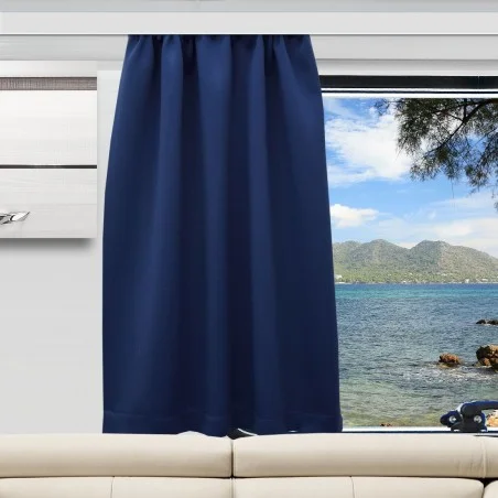 Ein dunkelblauer Vorhang verdeckt die Hälfte eines großen Fensters in einem modernen Wohnwagen. Durch das Fenster blickt man auf einen ruhigen blauen Ozean, Baumzweige und entfernte grüne Hügel unter einem teilweise bewölkten Himmel. Unter dem Fenster befindet sich ein beiges Sofa.