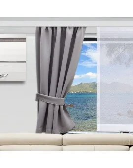 In einem modernen Wohnzimmer steht ein hellbeiges Sofa vor einem großen Fenster. Ein einzelner grauer Vorhang ist an der Seite befestigt und gibt den Blick auf das blaue Wasser, die felsige Küste und die grünen Hügel in der Ferne unter dem hellen Himmel frei.
