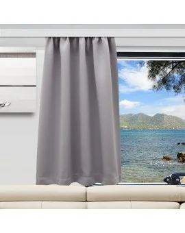 Ein grauer Vorhang ist bis zur Hälfte über ein Fenster gezogen und verdeckt teilweise den Blick auf das blaue Meer, die felsige Küste und die entfernten grünen Hügel unter einem teilweise bewölkten Himmel. Unter dem Fenster steht ein beiges Sofa, daneben hängt ein modernes Gemälde an der Wand.