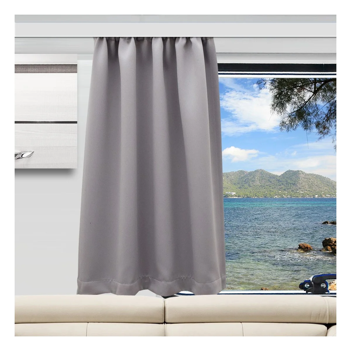 Ein grauer Vorhang ist bis zur Hälfte über ein Fenster gezogen und verdeckt teilweise den Blick auf das blaue Meer, die felsige Küste und die entfernten grünen Hügel unter einem teilweise bewölkten Himmel. Unter dem Fenster steht ein beiges Sofa, daneben hängt ein modernes Gemälde an der Wand.