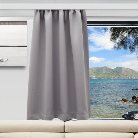 Ein grauer Vorhang ist bis zur Hälfte über ein Fenster gezogen und verdeckt teilweise den Blick auf das blaue Meer, die felsige Küste und die entfernten grünen Hügel unter einem teilweise bewölkten Himmel. Unter dem Fenster steht ein beiges Sofa, daneben hängt ein modernes Gemälde an der Wand.