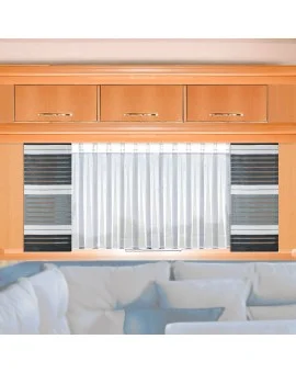Innenansicht eines Wohnwagenfensters mit dem weißen Caravan-Store ANNA, kombiniert mit der grauen Flächengardine AIKO; moderne Fensterausstattung im Camper mit Holzschrank und gemütlicher Sitzecke.