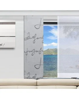 In einem modernen Wohnzimmer steht ein cremefarbenes Sofa vor einem Fenster. Aus dem Fenster blickt man auf blaues Wasser, grüne Hügel und einen teilweise bewölkten Himmel. Vorhänge mit handgeschriebener Schrift und ein durchsichtiges weißes Paneel sind teilweise über das Fenster gezogen.