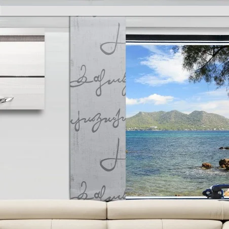 In einem Wohnzimmer stehen eine weiße Couch und ein grau gemusterter Vorhang, der ein großes Fenster teilweise verdeckt. Draußen sieht man das blaue Wasser des Ozeans, die felsige Küste, ferne Berge und einen teilweise bewölkten Himmel, an dem rechts oben Äste zu sehen sind.