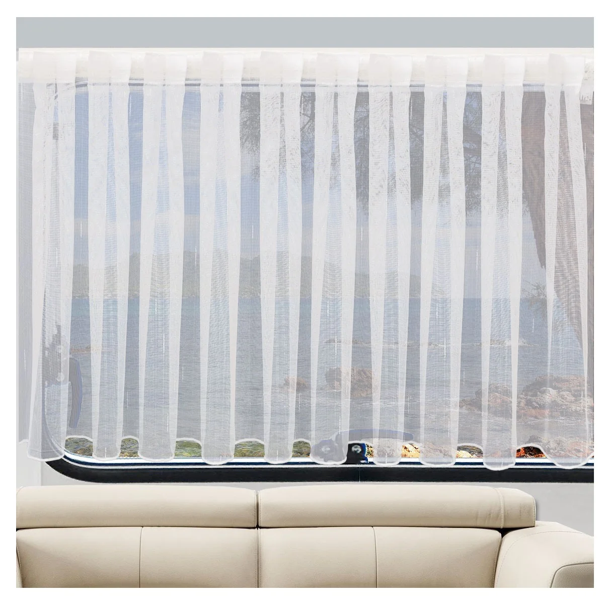 Ein durchsichtiger weißer Vorhang bedeckt ein Fenster und streut das einfallende Licht. Hinter dem Vorhang sind das Meer und eine felsige Küstenlinie zu sehen. Im Vordergrund, unterhalb des Fensters, ist ein Teil eines hellbeigen Sofas zu sehen.