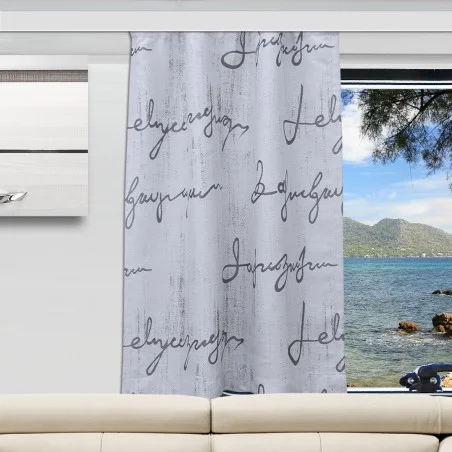 In einem modernen Wohnzimmer steht ein weißes Sofa vor einem Fenster. Ein Vorhangpaneel zeigt ein weißes und graues Holzmaserungsmuster mit schwarzem kursivem Text. Der Blick nach draußen umfasst das Meer, Berge, Bäume und einen Himmel mit vereinzelten Wolken.
