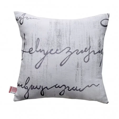 Quadratisches Zierkissen mit weißem Hintergrund und schwarzer, abstrakter Kursivschrift auf der Oberfläche. Die Schrift ist stilisiert und nicht als Text lesbar. An der linken Seite des Kissens ist ein kleines rotes Schildchen angebracht. Das Design ist modern und minimalistisch.