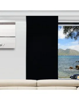 Ein schwarzer Vorhang ist an einem großen Fenster teilweise geöffnet und gibt den Blick auf den Ozean mit einer felsigen Küste und fernen Bergen unter einem klaren blauen Himmel frei. Im Inneren des Raums sind ein Teil eines cremefarbenen Sofas und ein modernes Wandkunstwerk zu sehen.