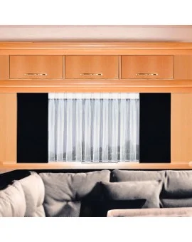 In einem Raum ist eine helle Holzwand mit drei Schränken über einem Fenster mit weißen Vorhängen angebracht. Schwarze Paneele begrenzen das Fenster. Ein graues Sofa mit schwarzen und grauen Kissen ist teilweise im Vordergrund zu sehen.