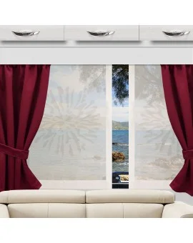 In einem Wohnmobil steht ein weißes Sofa vor einem Fenster, das von weinroten Vorhängen eingerahmt wird. Das Fenster bietet einen Blick auf einen ruhigen See, ferne Berge und Baumzweige. Auf dem Volant sind dekorative Muster zu sehen.