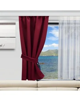 Ein weinroter Vorhang, der an einer Seite mit einem passenden Raffhalter befestigt ist, hängt neben einem durchsichtigen weißen Vorhang. Durch das Fenster sieht man blaues Wasser und in der Ferne grüne Hügel unter einem teilweise bewölkten Himmel. Im Vordergrund befindet sich ein weißes Sofa.