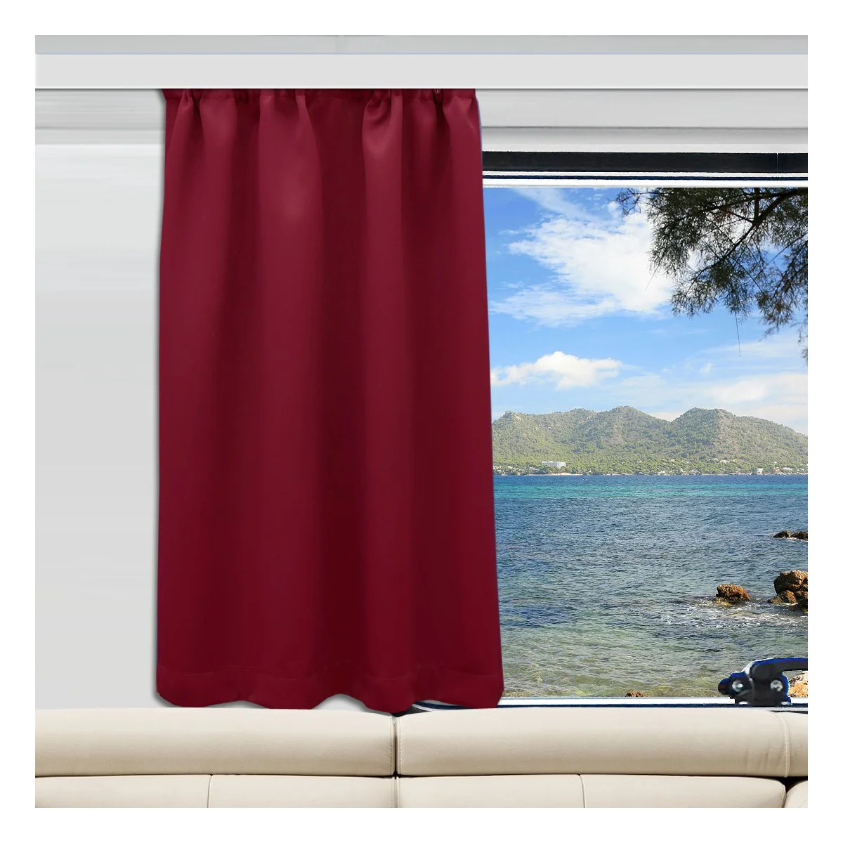 Ein weinroter Vorhang ist auf der linken Seite eines Fensters angebracht, das sich über einem weißen Sofa befindet. Durch das Fenster blickt man auf ein blaues Meer, grüne Hügel und einen teilweise bewölkten Himmel. Auf der rechten Seite des Rahmens ragt ein Baumzweig ins Bild.