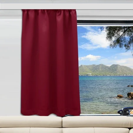 Ein weinroter Vorhang ist auf der linken Seite eines Fensters angebracht, das sich über einem weißen Sofa befindet. Durch das Fenster blickt man auf ein blaues Meer, grüne Hügel und einen teilweise bewölkten Himmel. Auf der rechten Seite des Rahmens ragt ein Baumzweig ins Bild.