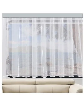 Ein durchsichtiger weißer Vorhang bedeckt ein großes Fenster, das teilweise den Blick auf einen ruhigen See, Berge und Bäume draußen versperrt. Das Fenster befindet sich hinter einem beigen Sofa in einem hellen Raum mit einer luftigen Atmosphäre.
